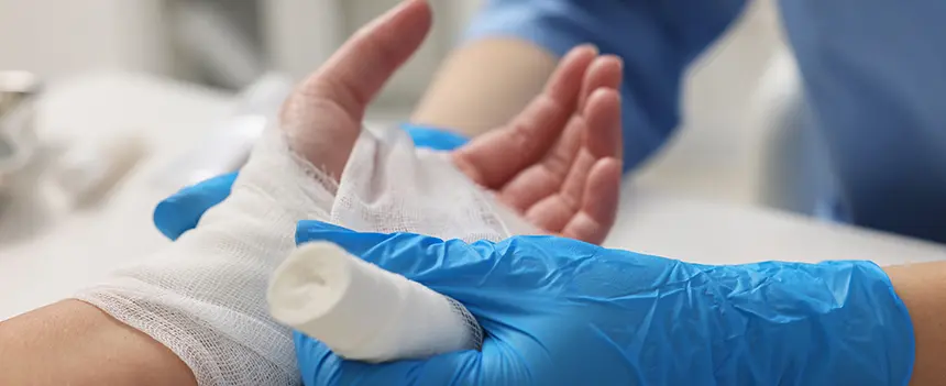 Arzt mit Handschuhen wickelt Zinkleimverband für ideale Wirkung vorsichtig um die Hand des Patienten